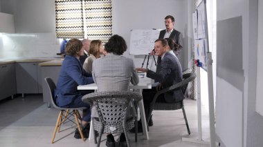Risk, analiz, pazarlama, fikirler ve iş stratejisi planlama konuları. Bir grup mutlu insan ofisteki bir masada oturuyor. Adam sunumu yönetiyor..