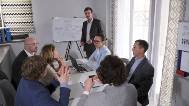 Bir grup girişimci çalışanları küçültmeyi tartışıyor. İş adamları ofisteki bir masada oturuyorlar. Adam sunumu yönetiyor. Sahne profesyonel ve odaklı.