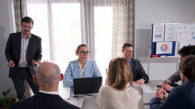 Bir adam bir grup işadamının önünde duruyor ve bir sunum yapıyor. Bir grupta insanlar arası ilişkiler kurmak. Sahne profesyonel ve ciddi.