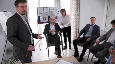 Bir koçtan akıl hocalığı. Ofisteki verimliliği ve takım çalışmasını arttırın. Bir grup insan bir odada sandalyede oturuyor ve bir akıl hocası beyaz tahtanın önünde duruyor..