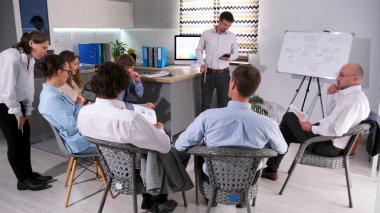 Bir şirket yöneticisinin başarılı bir iş fikri yaratma dersi. Davet edilen koç bir pazarlama sunumu yapar. Bir grup insan, arka planda beyaz pano olan bir hocanın etrafında oturuyorlar..