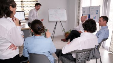 Bir grup işadamı beyaz bir kurulun etrafında toplandı, önünde bir öğretim görevlisi duruyor ve bir sunuma öncülük ediyor. Şirket aile ofisinde bir toplantı düzenler..