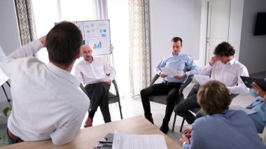 Genç başarılı girişimcilerin gayri resmi bir aile ofisinde buluşması. Bir grup adam bir akıl hocasının etrafında sandalyelerde oturuyor. Sahne ciddi ve odaklanmış.