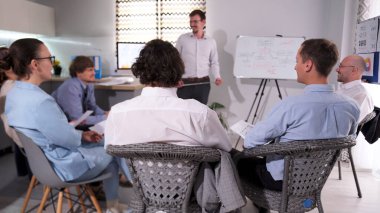 Yönetmenler toplantısı. Genç bir işletme şirketinde takım oluşturma. Akıl hocası liderlik gelişimi hakkında bir sunum yapar. Bir grup insan konferans odasında sandalyelerde oturuyor..