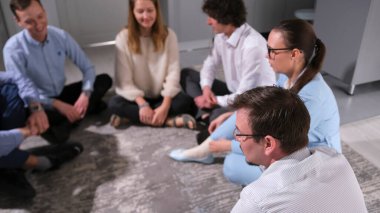 Meslektaşların birliği çemberi. Takım oluşturma ofis oyunları. Kişiler arası ilişkiler kurmak. Bir grup insan yerde oturup birbirleriyle sohbet ederken eğleniyorlar.