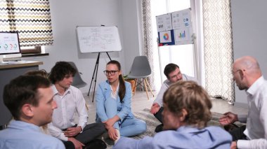 Uyumlu ve iyi etkileşimli bir ekip çalışmak için büyük bir motivasyon gösteriyor, bu da verimliliğin artmasına yol açıyor. Bir grup işadamı bir odada yerde oturuyorlar. Sahne takım çalışmasını temsil ediyor.