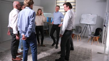 Birkaç başarılı meslektaş bir takım oluşturma etkinliği için bir araya geldi. Bir grup insan bir odada duruyor ve bir ofis oyununu tartışıyorlar.