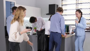 Bir grup aç ofis çalışanı mutfakta öğle yemeği yemek için toplandı. Aile ofisinde iş yemeği. Atmosfer rahat ve dost canlısı görünüyor, ve insanlar birbirlerinin arkadaşlığından hoşlanıyor..