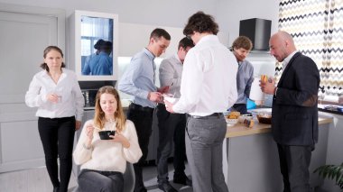 Samimi iş arkadaşları mutfakta toplandı, bazıları sandviç yiyor, bazıları kahve içiyor. Aile ofisinde iş yemeği. Atmosfer rahat görünüyor ve insanlar birbirlerinin arkadaşlığından hoşlanıyor..