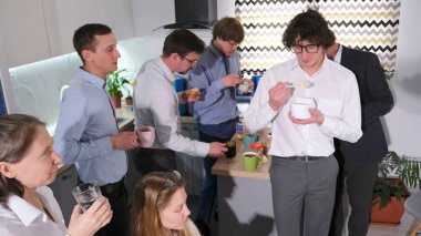 Şirket çalışanları öğle yemeği için mutfakta toplandılar. Aile ofisinde iş yemeği. Kahve molası veren bir ekip. Bir koçtan akıl hocalığı molası. Atmosfer rahat ve dost canlısı.