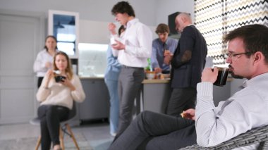 Bir takım oluşturma etkinliğinde bir misafir koç kahve molası sırasında kahve içer. Samimi bir mutfakta bir ofis. Aile ofisi. Bir grup insan mutfakta toplandı, bazıları içiyor ve yiyor.