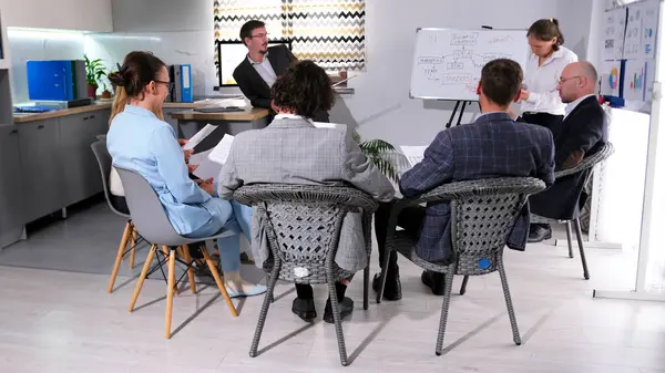 Pazarlamacıların toplantısı. Koçun sunumu. Akıl hocalığı. Bir grup iş adamı konferans odasında yarım daire şeklinde sandalyelerde oturuyorlar. Atmosfer profesyonel ve odaklı.