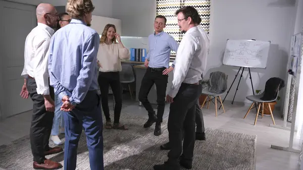 Birkaç başarılı meslektaş bir takım oluşturma etkinliği için bir araya geldi. Bir grup insan bir odada duruyor ve bir ofis oyununu tartışıyorlar.