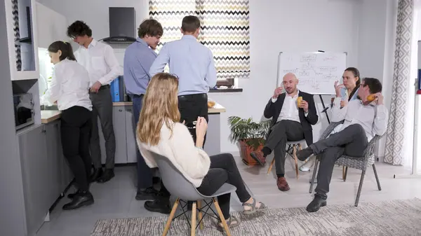 Sıcak bir aile ofisinde gayri resmi bir öğle yemeği. Bir grup iş adamı mutfakta toplandı, bazıları sandviç yiyor, diğerleri salata yiyor. Atmosfer rahat görünüyor, birbirlerinin arkadaşlığından hoşlanıyorlar..