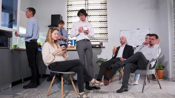 İş arkadaşları ofis mutfağında öğle yemeği yiyorlar. Aile ofisinde iş yemeği. Yorgun şirket çalışanları sandviç yiyor, salata yiyor ve kahve içiyor. Atmosfer rahat.