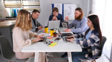 Takım çalışması. Profesyonellerden oluşan bir ekip toplantı odasında bir masada oturup dizüstü bilgisayarlar üzerinde çalışıyor. İş ofisi. Sahne odaklı ve üretken.