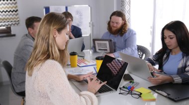 Tasarım bürosu önemli bir müşteri için yeni bir reklam kampanyası geliştiriyor. Bir grup insan dizüstü bilgisayarlarla bir masada oturuyor. Tasarımcıların günlük hayatı