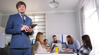 Gözlüklü ve mavi takım elbiseli gelecek vaat eden genç bir adam konferans odasında bir grup insanın önünde duruyor. O, elinde bir tablet tutuyor. Çalışanları dizüstü bilgisayarlarla dolu bir masada oturuyor.