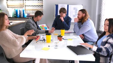 Bir grup insan konferans odasında bir masada oturuyor ve yeni bir iş geliştirme stratejisini tartışıyorlar. Aile ofisinde çalışan genç profesyoneller.