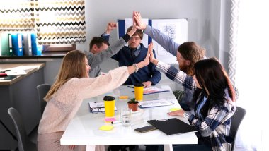 Bir grup genç iş adamı toplantı odasında bir masada oturup birbirlerine beşlik çakıyorlar. Sahne olumlu ve dostane. Başarılı bir alışveriş. Takım çalışması.
