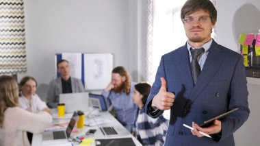 Başarılı bir modern şirkette çalışmak. Takım elbiseli mutlu bir adam benzer birini gösterir. Arkasında, bir grup meslektaşı bir masada oturuyor ve bir toplantı düzenliyor..