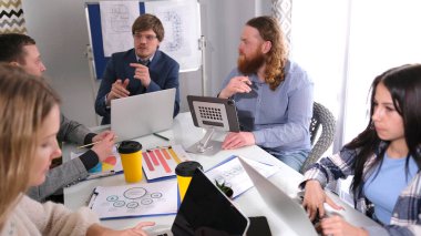 Şirketin müdürü astlarına görevleri dağıtır. - Evet. Genç profesyonellerden oluşan bir ekip bir girişim üzerinde çalışıyor. Bir grup insan bir dizüstü bilgisayarla bir masada oturuyor.