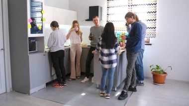 Gayri resmi giyinmiş ofis çalışanları ofis mutfağında öylesine sohbet ediyorlar. Kahve içip daha iyi bir gelecek hayal ediyorlar. İnsanlar birbirlerinin arkadaşlığından hoşlanırken manzara dostça..