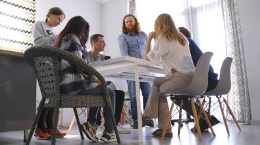 Takım oluşturma etkinliği. Davetli koç genç girişimciler için bir konferans görüyor. Birkaç kişi aile ofisindeki bir masanın etrafında oturuyor. Atmosfer rahat ve dost canlısı.