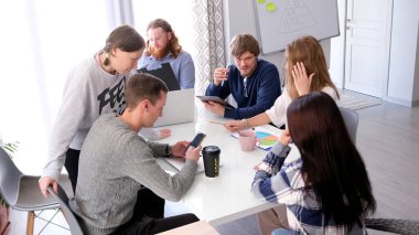 Bir grup meslektaşı yeni bir iş geliştirme stratejisi geliştiriyor. Genç girişimciler bir masaya oturup birlikte çalışırlar. Masada dizüstü bilgisayarlar var.