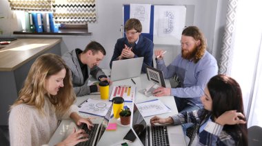 Tasarım ajansının çalışma günleri. Birçok yaratıcı insan ortak bir masada oturuyor ve dizüstü bilgisayarlarla ilgili bir proje üzerinde çalışıyorlar. Sabah brifingi