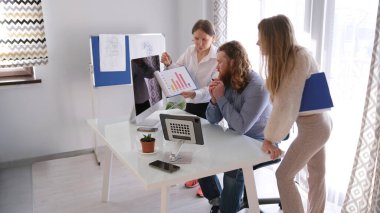 Üç iş adamı şirketin gelir çizelgesini tartışıyor. Kadın bir analist elinde diyagramı olan bir kağıt parçası tutuyor ve bir adam ona bakıyor. Sahne takım çalışmasını ve konsantrasyonunu temsil ediyor.