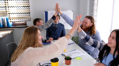 Küçük bir şirkette başarıyı kutlama konsepti. Bir grup öğrenci bir konferans odasında birbirleriyle coşkuyla sohbet ediyor ve birbirlerine beşlik çakıyorlar..