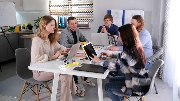 Yaratıcı arkadaşlardan oluşan bir ekip büyük bir ortak proje üzerinde çalışmak için aile ofisinde toplandı. Bir grup insan bir masada oturup dizüstü bilgisayarlar üzerinde çalışıyor..