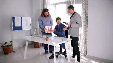 Müdürün özel danışmanı önemli bir toplantı hakkında onu bilgilendiriyor. Şirketin müdürü satış analizlerini yönetmenle tartışıyor. Sahne ciddi ve odaklanmış.