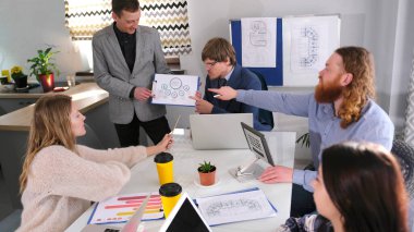 Bir grup insan toplantı için toplandı. Genç bir çalışan, şirketin gelişimini konu alan bir sunuma öncülük ediyor. Sahne ciddi ve odaklanmış.