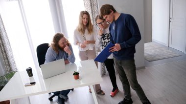 Bir grup arkadaş yeni bir iş geliştirme stratejisi geliştiriyor. Bir grup insan konferans odasındaki bir masanın etrafında duruyor. Sahne işbirlikçi ve odaklı.