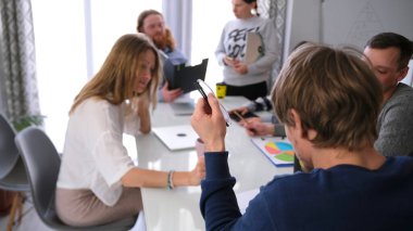Ofisteki takım çalışması süreci. Takım oluşturma ve beyin fırtınası. Bir grup insan toplantı odasında beyaz bir masada oturmuş ortak bir projeyi tartışıyorlar.