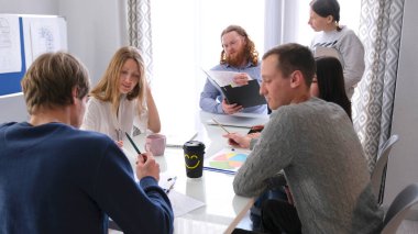 Şirketin müdürü, şirketin mevcut görevlerini astlarıyla tartışıyor. Bir grup insan bir masada oturuyor, bazıları ellerinde kağıt ve kalemler tutuyor..