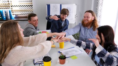 Yeni bir iş gününe hazır ol. Genç mutlu yöneticiler toplantı odasında masada otururken el sıkışıyorlar. Başarılı işbirliği kavramı