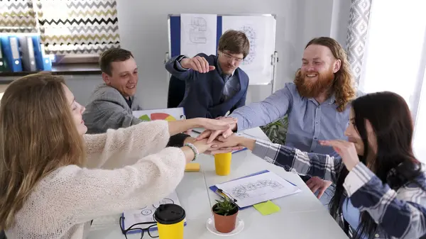 Yeni bir iş gününe hazır ol. Genç mutlu yöneticiler toplantı odasında masada otururken el sıkışıyorlar. Başarılı işbirliği kavramı