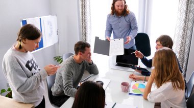 Takım çalışması. Takım oluşturma ve beyin fırtınası. Bir grup insan bir masada oturuyor, bir adam elinde bir kontrat tutuyor. Sahne ciddi ve odaklanmış.