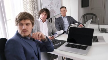 Üç erkek ekonomist toplantı odasında bir masada oturuyorlar. Yatırım yönetimi, risk değerlendirmesi ve finansal strateji geliştirme. Kârlılık analizi