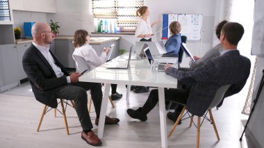 Aile ofisi. Bir grup girişimci konferans odasında bir masada oturuyor ve bir sunum panosuna bakıyor. Genç bir kadın ekonomist, şirketin giderleri ve gelirleri hakkında konuşuyor.