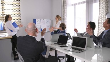 İş adamları, kadın meslektaşlarını finansal verileri başarılı bir şekilde analiz ettikleri için alkışlıyorlar. Bir grup ofis çalışanı toplantı odasında alkışlıyor. İyi bir anlaşma için tebrikler.