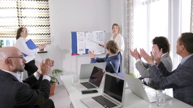 Ekonomi ekibi iş sunumunda öğretim üyesini alkışlıyor. Ekonomik bilgilerin toplanması, işlenmesi ve analizi. Bir grup insan başarılı bir iş fikrinin yaratılmasını kutluyor.