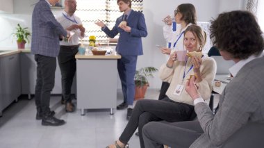İş arkadaşları ofis mutfağında öğle yemeği arasında birbirleriyle sohbet ederken eğleniyorlar. Bir grup insan sandviç yiyor ve kahve içiyor. İş yemeği..