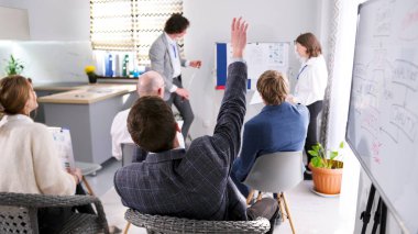 Bir adam ekonomi seminerindeki bir koça soru sormak için elini kaldırır. Küçük bir hukuk firması için takım çalışması. Bir grup insan konferans odasında konferansta.