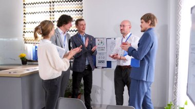 Mutlu meslektaşlar sunum kurulundaki konferans odasında birbirlerini alkışlıyorlar. Bir grup insan başarılı bir anlaşma yaptıkları için birbirlerini tebrik ediyorlar..