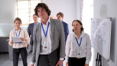 Tanıtımdan isim etiketli bir grup genç profesyonel ayrılıyor. Sahne ciddi ve odaklanmış. Pratik yapan öğrenciler. Aile ofisinde bir konferans odası..