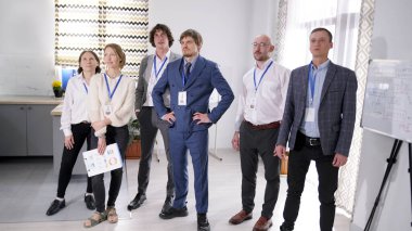 Farklı yaşlardan uzmanlardan oluşan komik bir ekip. Bir grup kadın ve erkek bir odada duruyor, bazıları takım elbiseli. Sahne profesyonel ve odaklı.